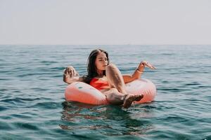 vrouw zomer zee. gelukkig vrouw zwemmen met opblaasbaar donut Aan de strand in zomer zonnig dag, omringd door vulkanisch bergen. zomer vakantie concept. foto