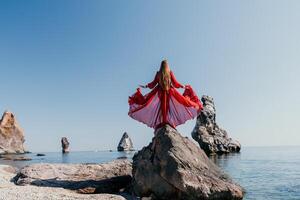 vrouw reizen zee. jong gelukkig vrouw in een lang rood jurk poseren Aan een strand in de buurt de zee Aan achtergrond van vulkanisch rotsen, Leuk vinden in IJsland, sharing reizen avontuur reis foto