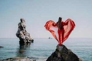vrouw reizen zee. jong gelukkig vrouw in een lang rood jurk poseren Aan een strand in de buurt de zee Aan achtergrond van vulkanisch rotsen, Leuk vinden in IJsland, sharing reizen avontuur reis foto
