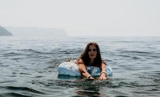 vrouw zomer zee. gelukkig vrouw zwemmen met opblaasbaar donut Aan de strand in zomer zonnig dag, omringd door vulkanisch bergen. zomer vakantie concept. foto