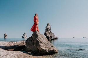 vrouw reizen zee. jong gelukkig vrouw in een lang rood jurk poseren Aan een strand in de buurt de zee Aan achtergrond van vulkanisch rotsen, Leuk vinden in IJsland, sharing reizen avontuur reis foto