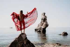 vrouw reizen zee. jong gelukkig vrouw in een lang rood jurk poseren Aan een strand in de buurt de zee Aan achtergrond van vulkanisch rotsen, Leuk vinden in IJsland, sharing reizen avontuur reis foto