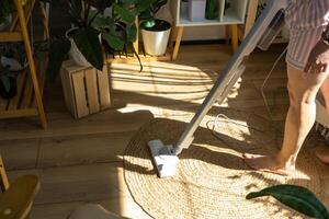 een vrouw stofzuigers een ronde tapijt in een huis tussen huis planten met een hand- vacuüm schoner. algemeen schoonmaak van de huis, schoonmaak onderhoud en huisvrouw foto