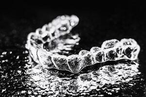 transparant aligners, tand vasthouders liggen Aan een spiegel met water druppels Aan een zwart achtergrond foto