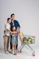 beeld van Aziatisch familie voortvarend een supermarkt kar terwijl winkelen, geïsoleerd Aan wit achtergrond foto