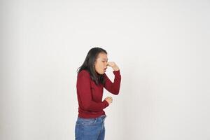 jong Aziatisch vrouw in rood t-shirt ruiken iets stinkend en walgelijk geïsoleerd Aan wit achtergrond foto