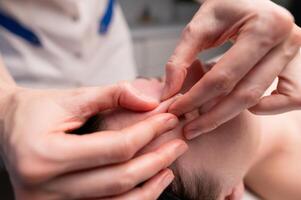 detailopname schot van een vrouw hoofd aan het doen een gelaats massage Aan een behandeling tafel. therapeut toepassen druk met duimen Aan voorhoofd foto