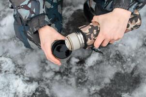 Mens giet een heet drinken buiten in winter. mannetje handen Holding thermosfles en mok, top visie detailopname foto