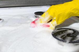vrouw hand- in handschoen schoonmaak gas- fornuis met spons met schuim. overvloedig schuim van chemisch schoonmaak vloeistof. foto