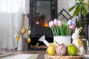 Pasen decor in de buurt haard fornuis met brand en brandhout. knus huis haard in interieur met ingemaakt plannen, kleurrijk Pasen eieren, Pasen konijn en boeket. voorjaar in een land huis foto