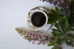 een kop van koffie en lupine bloemen Aan een wit houten tafel. foto