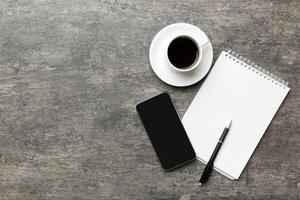 modern kantoor bureau tafel met notitieboekje, smartphone en andere benodigdheden met kop van koffie. blanco notitieboekje bladzijde voor u ontwerp. top visie, vlak leggen foto