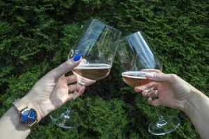 een glas van wijn in vrouwen handen tegen een natuurlijk achtergrond. twee vrienden juichen. drinken wijn. foto