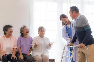 Aziatisch jong verpleegster ondersteuning senior ouder Mens wandelen met wandelaar. mooi verpleegster helpen en nemen zorg. ouderen volwassen opa geduldig aan het doen fysiek behandeling met een groep van senior vrienden in ziekenhuis. foto