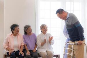 Aziatisch jong verpleegster ondersteuning senior ouder Mens wandelen met wandelaar. mooi verpleegster helpen en nemen zorg. ouderen volwassen opa geduldig aan het doen fysiek behandeling met een groep van senior vrienden in ziekenhuis. foto