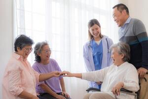 Aziatisch jong verpleegster ondersteuning paar senior ouder Mens en vrouw in een rolstoel. ouderen volwassen en een groep van senior vrienden leven in de ziekenhuis. gezelligheid van gepensioneerd mensen. foto