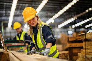 vrouw schoonmaak hout hout in donker magazijn industrie. team arbeider timmerman vervelend veiligheid uniform en moeilijk hoed werken en controle de kwaliteit van houten producten Bij werkplaats productie. foto