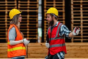 arbeiders timmerman vervelend veiligheid uniform en moeilijk hoed werken en controle de kwaliteit van houten producten Bij werkplaats productie. Mens en vrouw arbeiders hout in donker magazijn industrie. foto