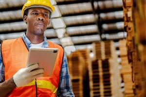 Afrikaanse arbeider timmerman vervelend veiligheid uniform en moeilijk hoed werken en controle de kwaliteit van houten producten Bij werkplaats productie. Mens en vrouw arbeiders hout in donker magazijn industrie. foto