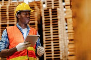 Afrikaanse arbeider timmerman vervelend veiligheid uniform en moeilijk hoed werken en controle de kwaliteit van houten producten Bij werkplaats productie. Mens en vrouw arbeiders hout in donker magazijn industrie. foto