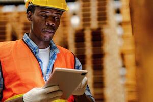 Afrikaanse arbeider timmerman vervelend veiligheid uniform en moeilijk hoed werken en controle de kwaliteit van houten producten Bij werkplaats productie. Mens en vrouw arbeiders hout in donker magazijn industrie. foto