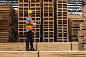 Afrikaanse arbeiders Mens bouwkunde wandelen en inspecteren met werken suite jurk en hand- handschoen in hout hout magazijn. concept van slim industrie arbeider werkend. hout fabrieken produceren hout gehemelte. foto