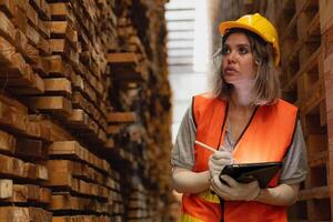 vrouw arbeider timmerman vervelend veiligheid uniform en moeilijk hoed werken en controle de kwaliteit van houten producten Bij werkplaats productie. Mens en vrouw arbeiders hout in donker magazijn industrie. foto