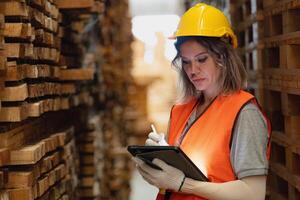 vrouw arbeider timmerman vervelend veiligheid uniform en moeilijk hoed werken en controle de kwaliteit van houten producten Bij werkplaats productie. Mens en vrouw arbeiders hout in donker magazijn industrie. foto