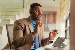 klant ondersteuning telefoontje centrum operator of receptioniste. klant onderhoud en Mens consultant pratend terwijl aan het doen een overleg online. Afrikaanse operator mannetje telemarketing middel Aan een laptop in kantoor foto