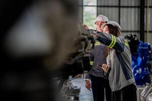 fabriek ingenieur vrouw inspecteren Aan machine met slim tablet. arbeider werken Bij machine robot arm. de lassen machine met een afgelegen systeem in een industrieel fabriek. kunstmatig intelligentie- concept. foto