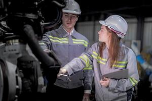 bedrijf ingenieurs ontmoeten en controleren controle zwaar machine robot arm. verschillend team van industrieel robotica ingenieurs verzameld in de omgeving van machine. professioneel machinerie operator gebruik industrieel digitaal tablet. foto