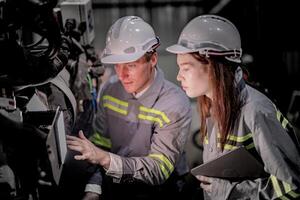 bedrijf ingenieurs ontmoeten en controleren controle zwaar machine robot arm. verschillend team van industrieel robotica ingenieurs verzameld in de omgeving van machine. professioneel machinerie operator gebruik industrieel digitaal tablet. foto