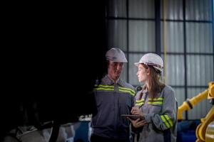 fabriek ingenieur vrouw inspecteren Aan machine met slim tablet. arbeider werken Bij machine robot arm. de lassen machine met een afgelegen systeem in een industrieel fabriek. kunstmatig intelligentie- concept. foto