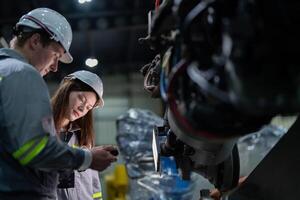 fabriek ingenieur vrouw inspecteren Aan machine met slim tablet. arbeider werken Bij machine robot arm. de lassen machine met een afgelegen systeem in een industrieel fabriek. kunstmatig intelligentie- concept. foto