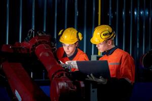 groep van mannetje ingenieur arbeiders onderhoud automatisch robot arm machine in een donker kamer fabriek. arbeider controle en repareren automatisch robot hand- machine. arbeider vervelend veiligheid bril en helm. foto