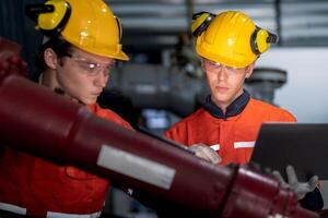 groep van mannetje ingenieur arbeiders onderhoud automatisch robot arm machine in een donker kamer fabriek. arbeider controle en repareren automatisch robot hand- machine. arbeider vervelend veiligheid bril en helm. foto