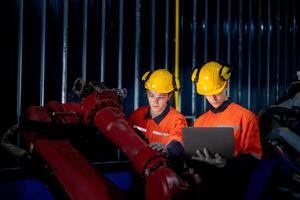 groep van mannetje ingenieur arbeiders onderhoud automatisch robot arm machine in een donker kamer fabriek. arbeider controle en repareren automatisch robot hand- machine. arbeider vervelend veiligheid bril en helm. foto