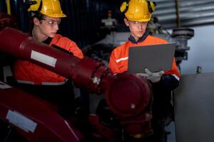 groep van mannetje ingenieur arbeiders onderhoud automatisch robot arm machine in een donker kamer fabriek. arbeider controle en repareren automatisch robot hand- machine. arbeider vervelend veiligheid bril en helm. foto