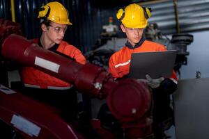 groep van mannetje ingenieur arbeiders onderhoud automatisch robot arm machine in een donker kamer fabriek. arbeider controle en repareren automatisch robot hand- machine. arbeider vervelend veiligheid bril en helm. foto