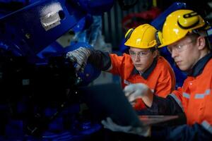 fabriek ingenieurs inspecteren Aan machine met slim tablet. arbeider werken Bij zwaar machine robot arm. de lassen machine met een afgelegen systeem in een industrieel fabriek. kunstmatig intelligentie- concept. foto