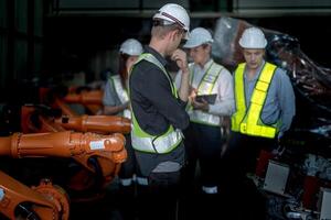 verkoop manager en fabriek eigenaar in pakken onderhandelen verkoop robots gebruikt in de fabriek. bedrijf ingenieurs vergadering en controle nieuw machine robot. arbeiders wandelen Bij magazijn lassen machine. foto