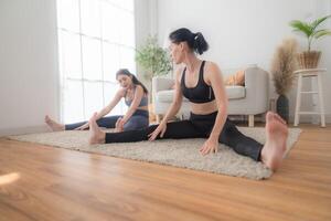 twee Dames zelfverzekerd opleiding yoga. atletisch Dames in sportkleding aan het doen geschiktheid uitrekken opdrachten Bij huis in de leven kamer. sport en recreatie concept. yoga leraar is helpen jong vrouw. foto