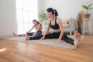 twee Dames zelfverzekerd opleiding yoga. atletisch Dames in sportkleding aan het doen geschiktheid uitrekken opdrachten Bij huis in de leven kamer. sport en recreatie concept. yoga leraar is helpen jong vrouw. foto