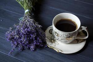 een kop van koffie, boeket van lavendel en toetje Aan donker blauw houten tafel. foto