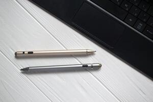 goud en zilver stylus pennen met toetsenbord Aan een wit houten achtergrond dichtbij omhoog. foto