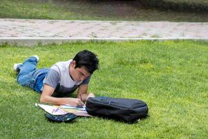 een mannetje leerling aan het liegen Aan de gras schrijven Aan een stuk van papier foto