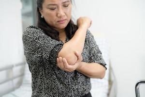 aziatische dame van middelbare leeftijd vrouw patiënt aanraken en voelen pijn haar elleboog en arm, gezond medisch concept. foto