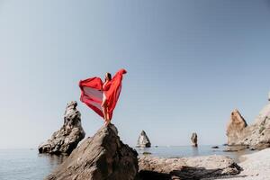 vrouw reizen zee. jong gelukkig vrouw in een lang rood jurk poseren Aan een strand in de buurt de zee Aan achtergrond van vulkanisch rotsen, Leuk vinden in IJsland, sharing reizen avontuur reis foto