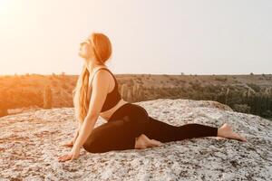 geschiktheid vrouw. gelukkig middelbare leeftijd geschiktheid vrouw aan het doen uitrekken en pilates Aan een rots in de buurt Woud Bij zonsondergang. vrouw geschiktheid yoga routine. gezond levensstijl met focus Aan welzijn en ontspanning. foto