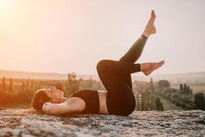 geschiktheid vrouw. gelukkig middelbare leeftijd geschiktheid vrouw aan het doen uitrekken en pilates Aan een rots in de buurt Woud Bij zonsondergang. vrouw geschiktheid yoga routine. gezond levensstijl met focus Aan welzijn en ontspanning. foto